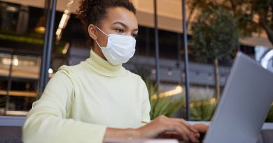 Low angle portrait of Asian young woman wearing mask and using laptop while working at table in cafe