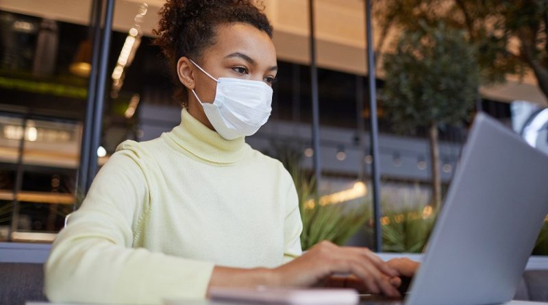 Low angle portrait of Asian young woman wearing mask and using laptop while working at table in cafe